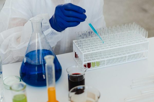Scientist in protective gear handling colorful liquids in a lab setting for research.